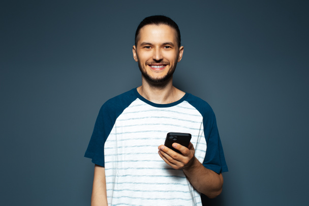 Studio portrait of young smiling man, holding a smartphone.   - 写真・画像