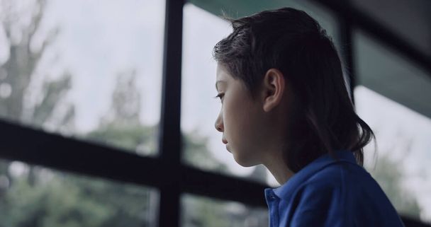 Boldogtalan iskolás fiú néz ablak ülő terem közelről. A stresszes kamaszfiú üres sötét folyosón kel fel. Magányos gyerek, aki magányosnak érzi magát az iskolában. Csak egy szomorú tinédzser portréja.. - Fotó, kép
