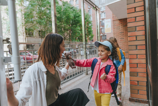 Happy smiling woman teacher greeting elementary school student at first day at school standing near the open door outside. Selective focus. - 写真・画像