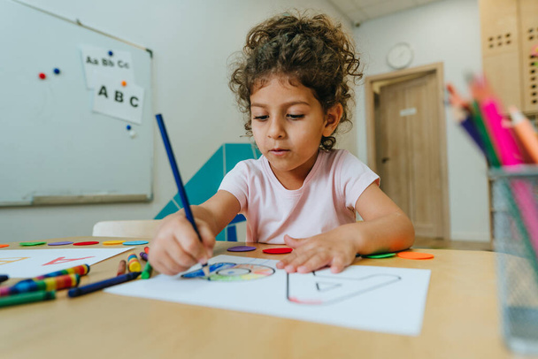 English lesson at elementary school or kindergarten. Girl learning the alphabet and colors coloring the letter A. Selective focus. - Φωτογραφία, εικόνα