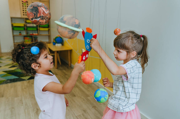 Little girl playing with paper spaceship learning Solar system planets models at home or kindergarten. Education science concept. Selective focus. - 写真・画像