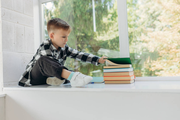 A schoolboy sits on the windowsill with books to read - Photo, Image