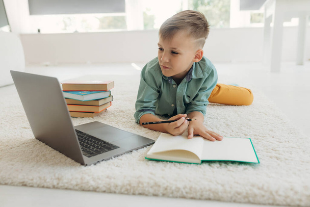 Schoolboy works with laptop while doing homework at home - Fotoğraf, Görsel