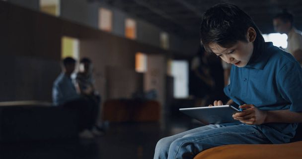 Nastoletni uczeń gra online na przerwie w szkole. Mały chłopiec korzystający z tabletu surfing web sam siedzi na ławce. Skupiony facet ignorujący przyjaciół. Koncepcja uzależnienia od technologii dla dzieci. - Zdjęcie, obraz