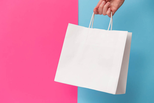 Female hand holding white blank shopping bag isolated on pink and blue background. Black friday sale, discount, recycling, shopping and ecology concept - Foto, imagen