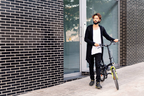young caucasian man leaving his front door walking with his bike, concept of urban lifestyle and sustainable mobility, copy space for text - 写真・画像