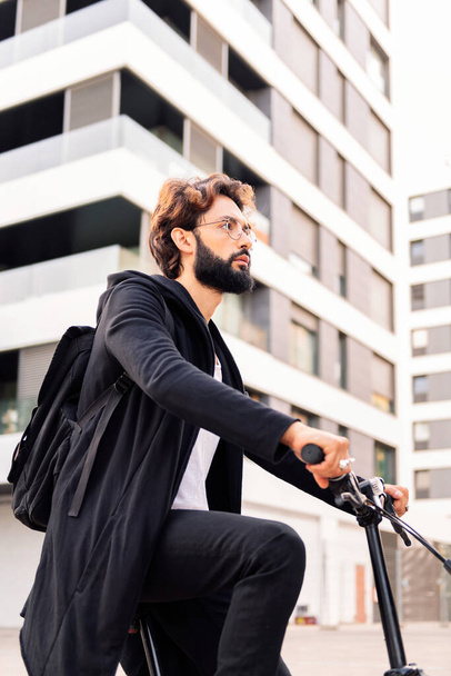 stylish young bearded man riding his bike through the city, concept of urban lifestyle and sustainable mobility, copy space for text - Φωτογραφία, εικόνα