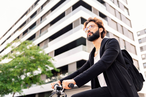 stylish young bearded man riding his bike through the city, concept of urban lifestyle and sustainable mobility, copy space for text - Фото, зображення