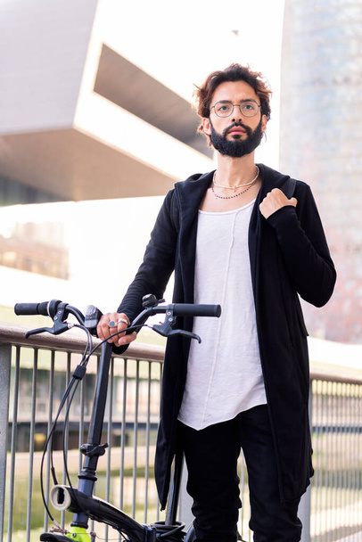 young caucasian man with beard wearing trendy clothes and walking with his folding bike through the city, concept of urban lifestyle and sustainable mobility - Fotoğraf, Görsel