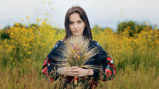 Portrait of beautiful sensual woman girl stylish caucasian lady wears ukrainian traditional patterned black dress stand in nature field posing with wildflowers hold at hands flowers bouquet dry grass - Fotografie, Obrázek