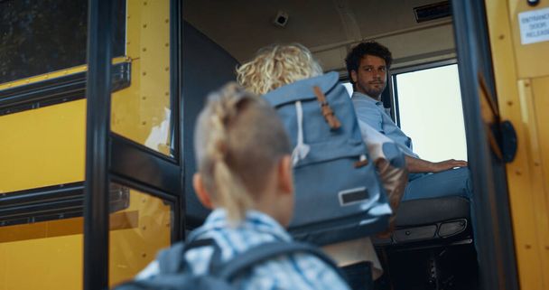Multi etnické děti nastupují do žlutého školního autobusu. Soustředěný řidič kontroluje žáky. Energeticky různorodé žáci základního věku jít nahoru v akademickém raketoplánu. Koncept veřejného vzdělávání. - Fotografie, Obrázek