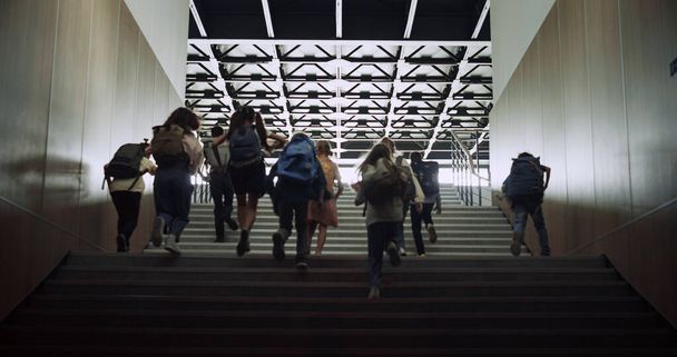 Energetische Teenager rennen im Schulflur nach oben. Schulkinder verlassen nach dem Unterricht das Schulgebäude. Gruppe verschiedener Schüler mit Rucksäcken stürmt Treppe. - Foto, Bild