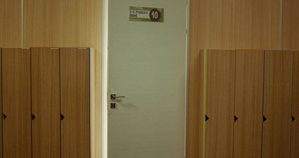 Κοντινό πλάνο της λευκής πόρτας της τάξης ανοιχτή σε άδεια αίθουσα. Σχολή διάδρομο εσωτερικό με ξύλινα ντουλάπια στη σειρά. Αποκάλυψαν την είσοδο της αίθουσας μελέτης στο μεσαίο διάδρομο. Καλοκαιρινές διακοπές. Εκπαιδευτική έννοια.  - Φωτογραφία, εικόνα
