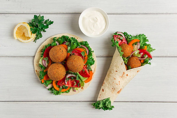 Tortillas, wrapped falafel balls, with fresh vegetables, vegetarian healthy food, on a wooden white background, no people, selective focus. - Photo, Image