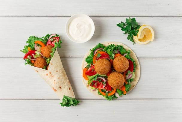 Tortillas, wrapped falafel balls, with fresh vegetables, vegetarian healthy food, on a wooden white background, no people, selective focus. - Foto, Bild