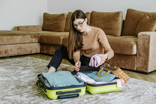 Travel fashion. Holiday beach. Beach bag. Happy young woman packing travel suitcase on floor at home. Vacation preparation. Tourist trip. - Photo, Image