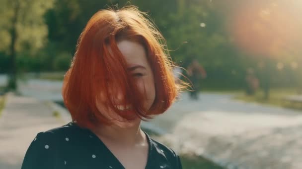 Portrait happy pretty caucasian red-haired beautiful attractive young girl student woman with short fluttering hair active moving flirting having good mood resting outdoors in park rejoicing weekend - Felvétel, videó