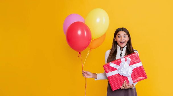 amazed child with party colorful balloons and present box on yellow background. - Foto, afbeelding