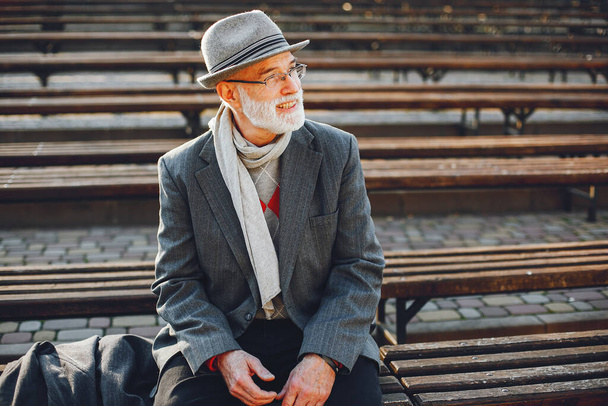 Handsome grandfather in a autumn park. Old man in a gray jacket and hat. Male sitting on the bench - Foto, immagini
