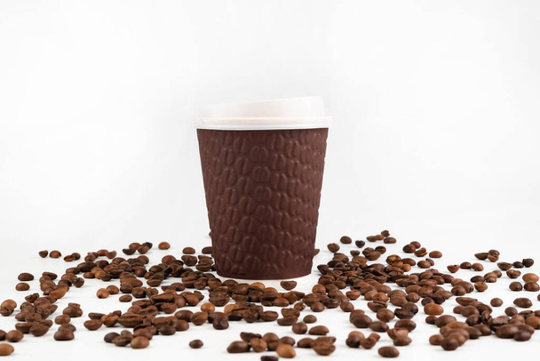 On a white background with coffee beans there is a disposable tableware with coffee. - Photo, image