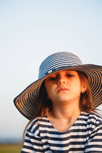 Close up portrait of little serious girl in blue and white striped sun hat and shirt looking at camera. Selective focus - Photo, Image