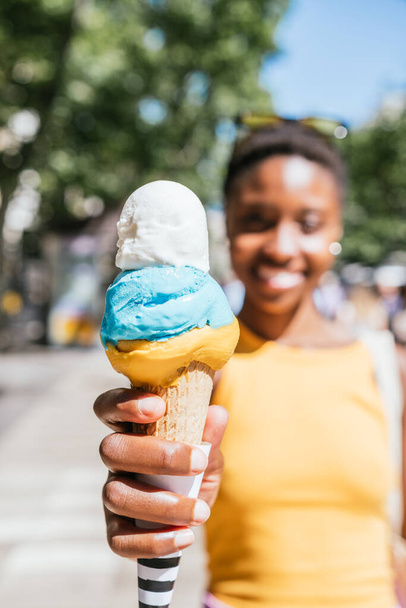 close up of a colorful ice-cream cone on the hands of an unrecognizable african woman - Zdjęcie, obraz