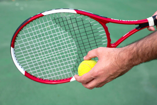 In the men's hands are a tennis racket and a ball against the background of a tennis court. - Foto, Bild