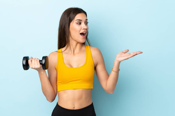 Young caucasian woman making weightlifting isolated on blue background with surprise facial expression - Foto, Imagen