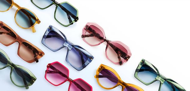 Sunglasses composition in many bright colors in transparent plastic. Top view with shadow. Trendy glasses isolated on white background. Glasses with polarized lenses. Fashionable eyewear for women. - 写真・画像