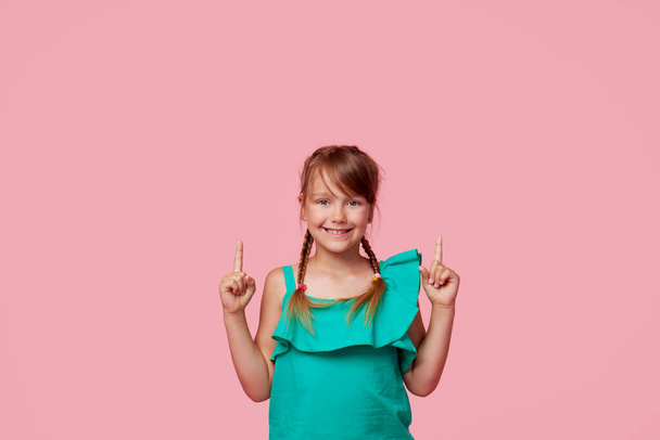 Portrait of cute toddler girl child with two funny pigtails over pink background. Points hands to the up side. Advertising childrens products - Foto, Imagen