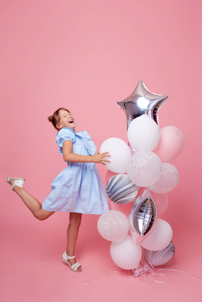 Joyful child girl in elegant tulle dress near the balloons. Birthday present. Funny face celebrates birthday party on pink background	 - Foto, afbeelding