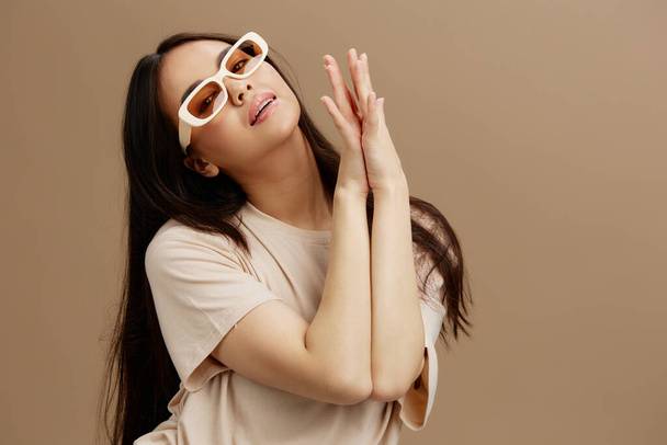 Portret kobiety w okularach przeciwsłonecznych T-shirt pozowanie nowoczesne style beżowe tło. Wysokiej jakości zdjęcie - Zdjęcie, obraz