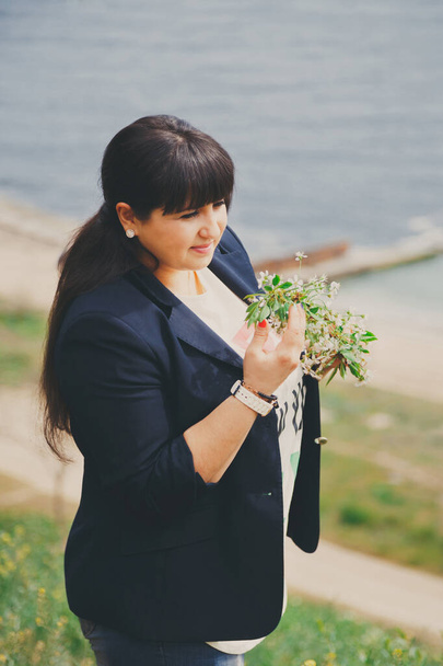 Happy smiling beautiful overweight young woman in dark blue jacket outdoors near to the sea with flowers. Confident fat young woman. Xxl woman, plus size woman on nature - Foto, Imagem