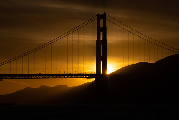 Sunset behind the Golden Gate Bridge.  Bright golden yellow against the silhouette of the bridge - 写真・画像