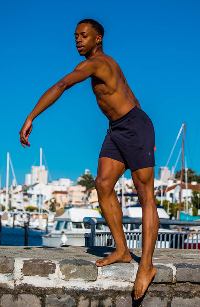 Ballet dancer with blue ocean water and sailboats behind him - Foto, immagini