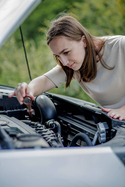 The woman pulls out a probe in her car engine to check the oil level. The woman manages the car herself. - Foto, Bild