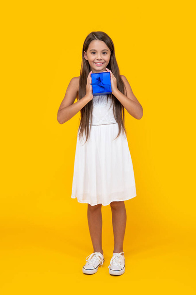 cheerful teen kid hold present box on yellow background. - Foto, afbeelding