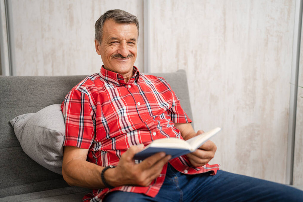 One man senior caucasian male with mustaches read book at home wear red shirt real people leisure concept copy space happy smile looking to the camera - Photo, Image
