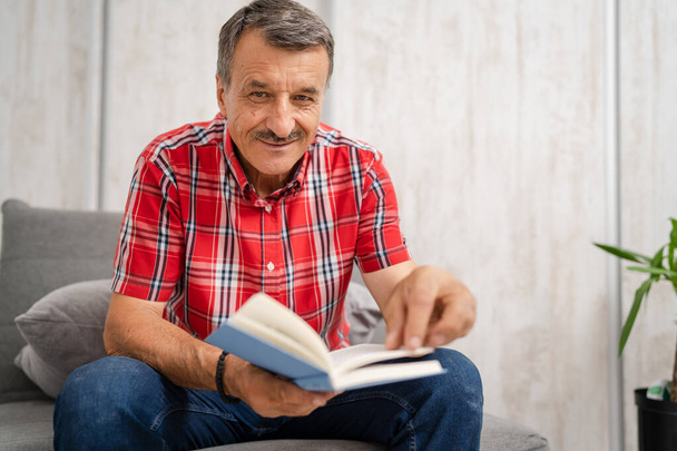 One man senior caucasian male with mustaches read book at home wear red shirt real people leisure concept copy space looking to the camera happy smile - Fotoğraf, Görsel