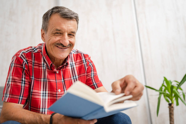 One man senior caucasian male with mustaches read book at home wear red shirt real people leisure concept copy space looking to the camera happy smile - 写真・画像