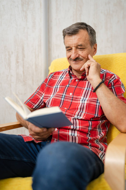 One man senior caucasian male with mustaches read book at home wear red shirt real people leisure concept copy space - Fotoğraf, Görsel