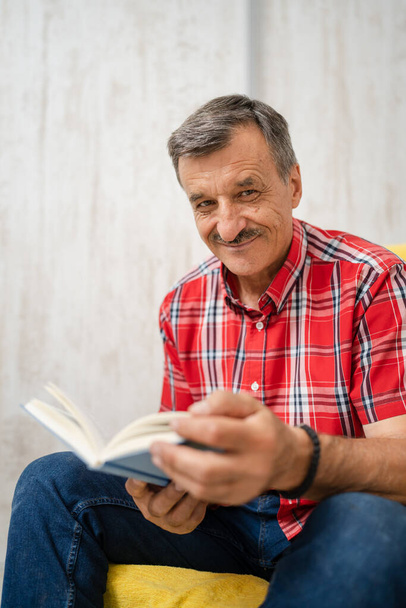 One man senior caucasian male with mustaches read book at home wear red shirt real people leisure concept looking to the camera copy space - 写真・画像