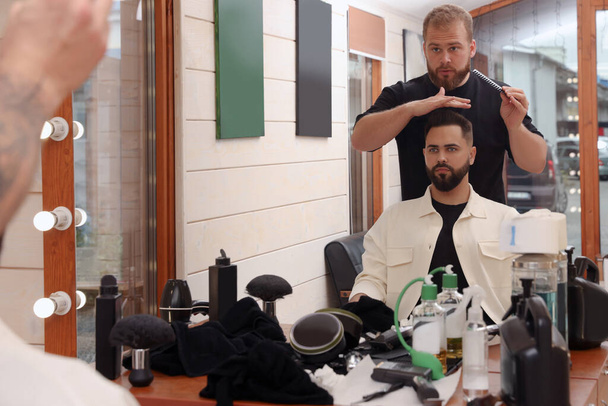 Professional hairdresser working with bearded client in barbershop - Фото, зображення