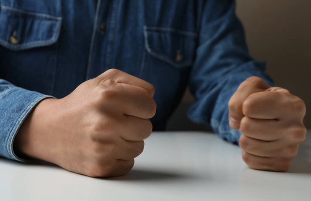 Man clenching fists at table while restraining anger, closeup - Valokuva, kuva