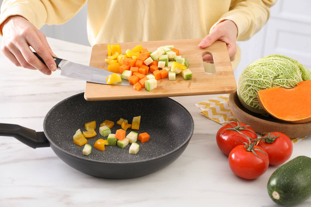 Vrouw gieten mix van gesneden groenten in koekenpan aan tafel in de keuken, close-up - Foto, afbeelding