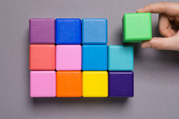 Woman holding wooden cube near others on grey background, top view. Management concept - Foto, afbeelding