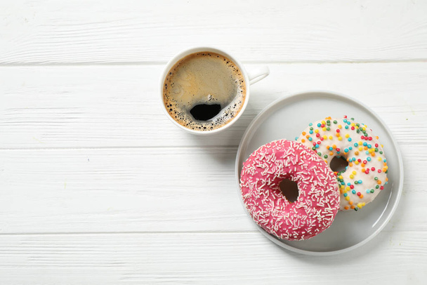 Yummy donuts with sprinkles and coffee on white wooden table, flat lay. Space for text - 写真・画像