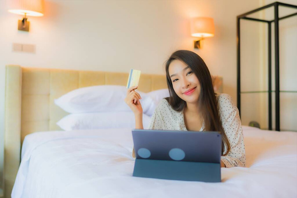 Πορτρέτο όμορφη νεαρή ασιατική γυναίκα χρησιμοποιούν tablet με πιστωτική κάρτα στο κρεβάτι στο εσωτερικό του υπνοδωματίου - Φωτογραφία, εικόνα