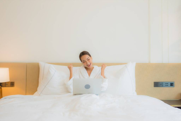 Πορτρέτο όμορφη νεαρή Ασιάτισσα γυναίκα χρησιμοποιούν φορητό υπολογιστή στο κρεβάτι στο εσωτερικό του υπνοδωματίου - Φωτογραφία, εικόνα