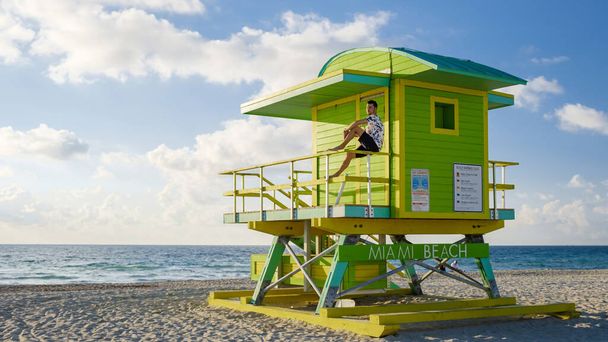 Майами Бич, молодые люди на пляже, спасатель хижина Майами Бич Флорида. Кавказские мужчины на пляже во время восхода солнца. Кавказцы расслабляются, наблюдая за океаном - Фото, изображение